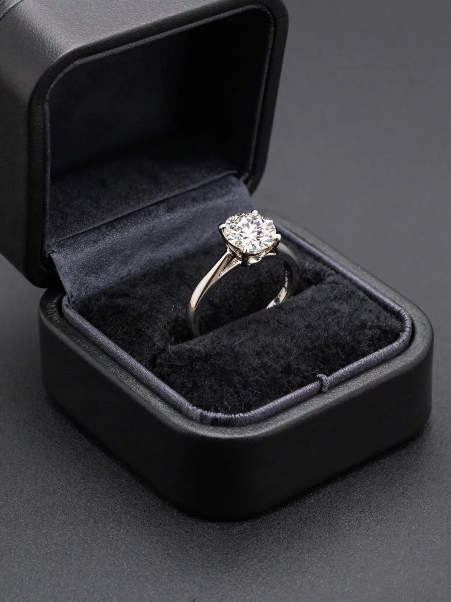 A solitaire engagement ring standing in an open black ring box