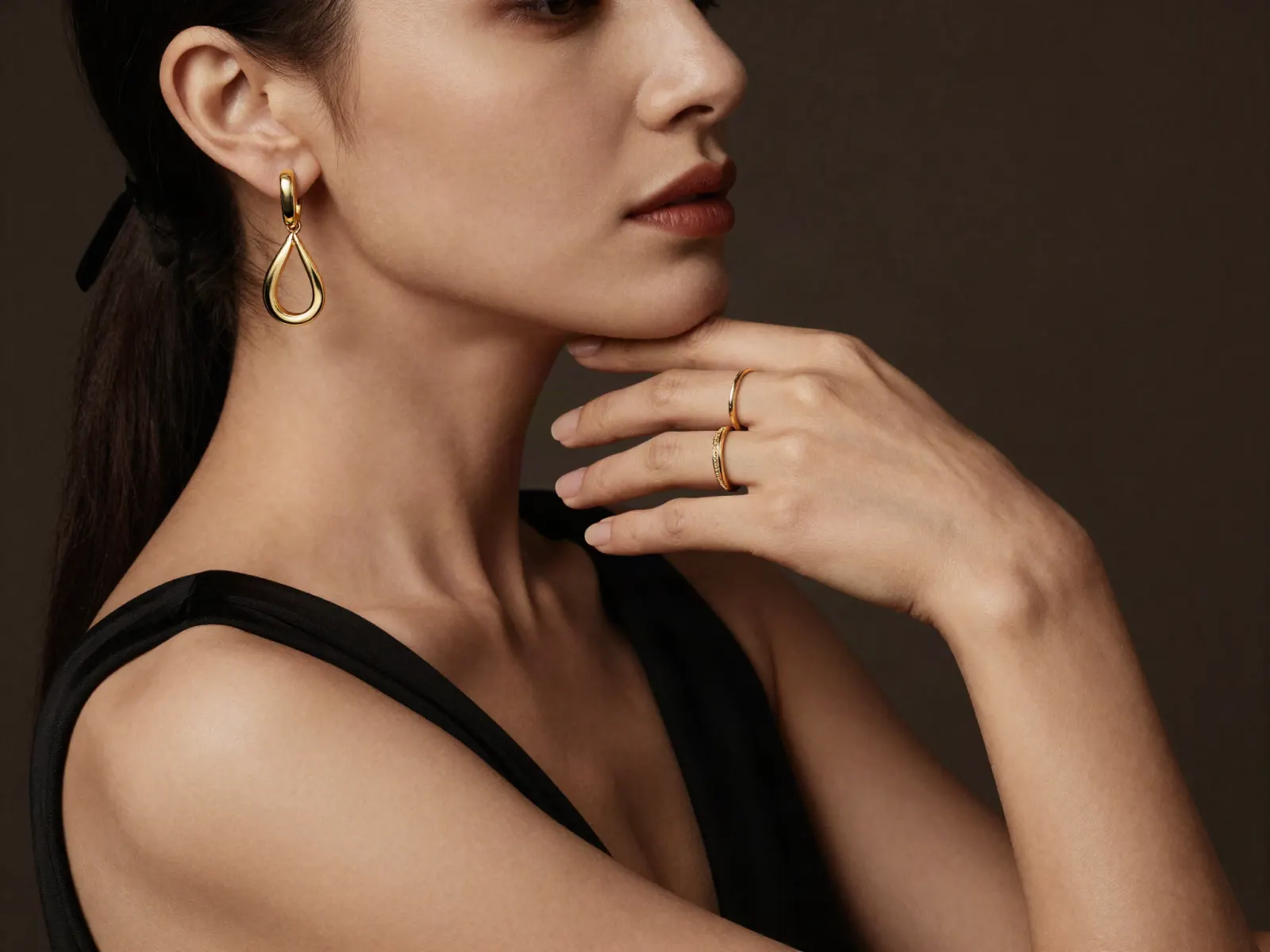 A woman in black wearing a gold teardrop earring and two slim gold rings