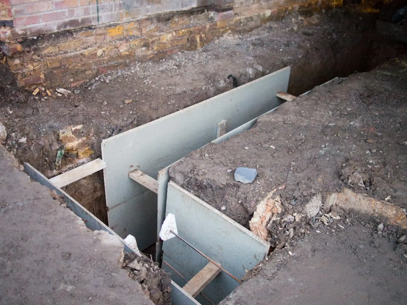 An excavated trench along a brick foundation, shored and ready for waterproofing