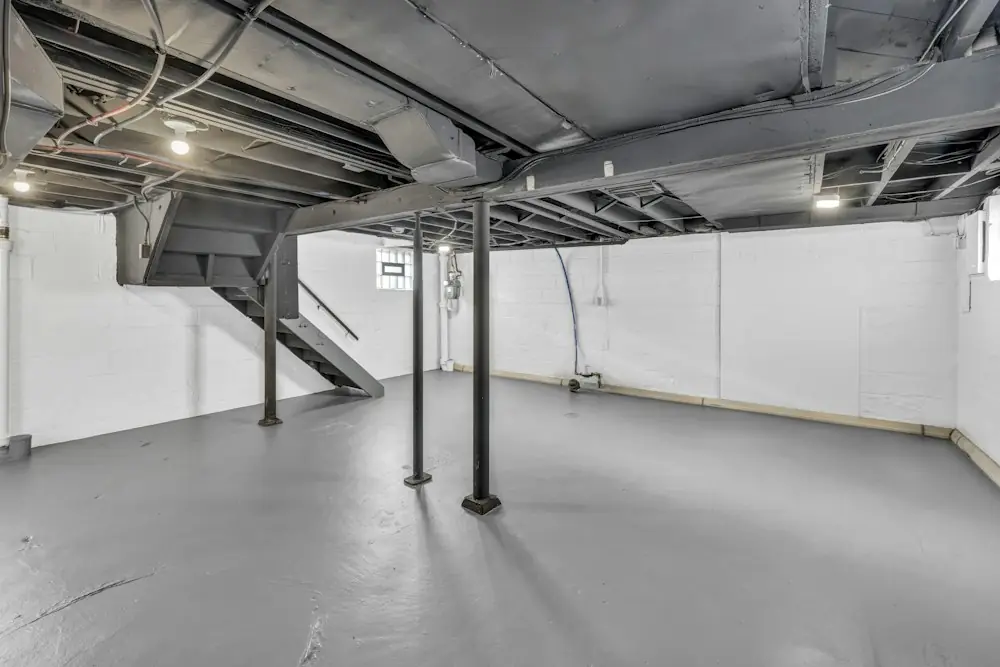 A dry, open basement with steel posts and exposed joists